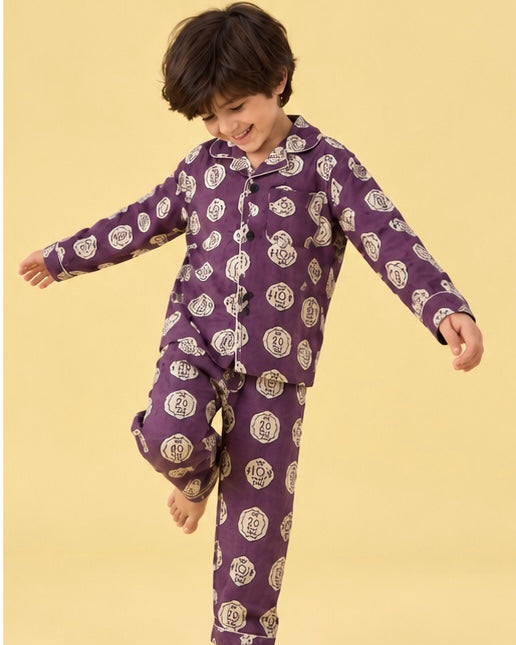 A young boy wearing a purple long-sleeve pajama set with a white circular pattern, posing on a solid pale yellow background.