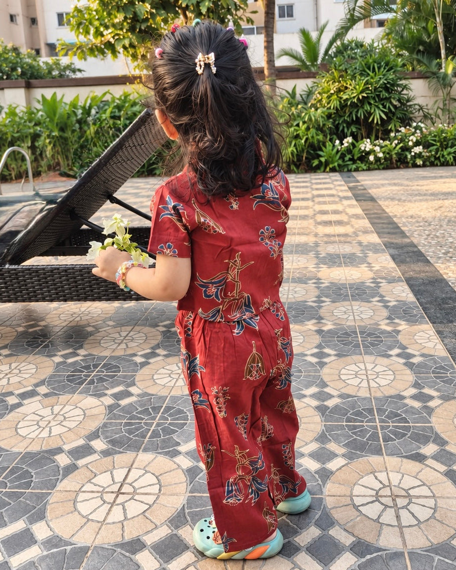 A young child viewed from behind wearing a red short-sleeve jumpsuit with a colorful butterfly print, standing on a tiled poolside patio.