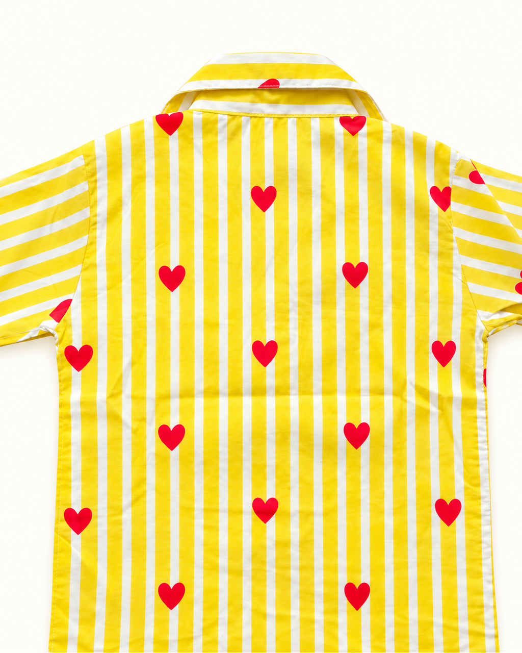 A yellow and white vertically striped short-sleeve button-up shirt with scattered red heart motifs, laid flat against a white background.