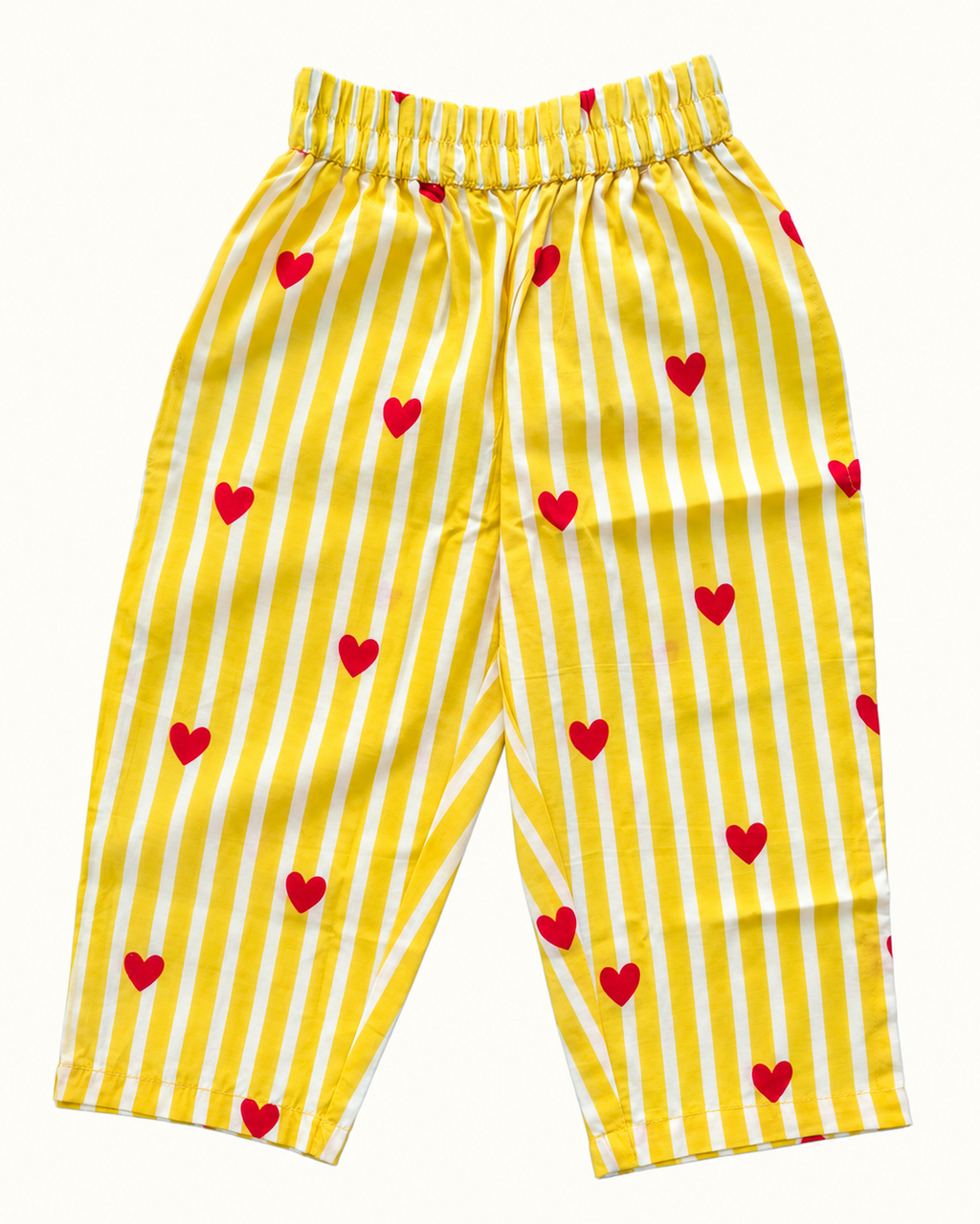 Yellow and white striped pants with small red hearts, featuring an elastic waistband, laid flat on a light cream background.
