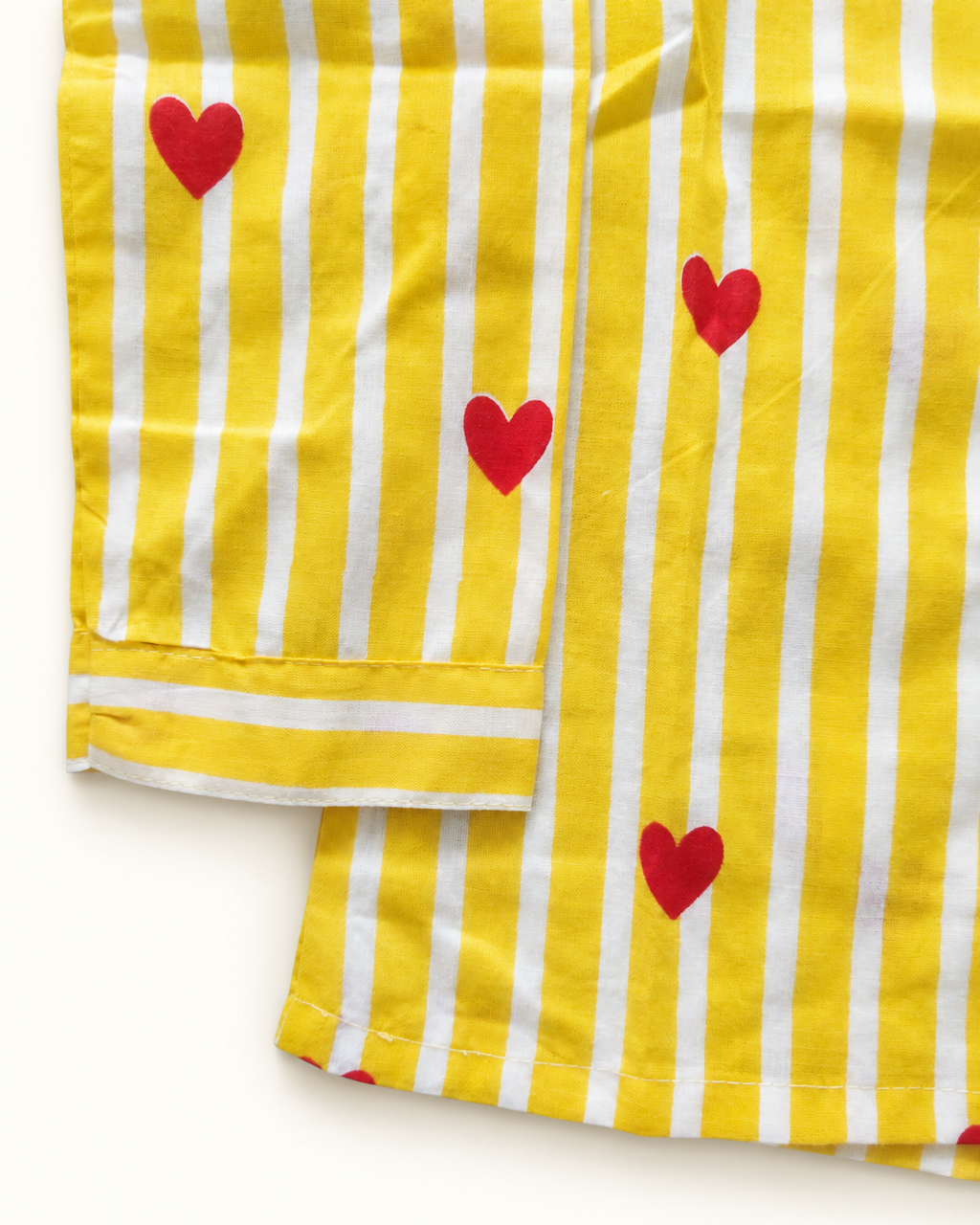 Yellow and white striped fabric with red heart prints, shown folded on a white background.