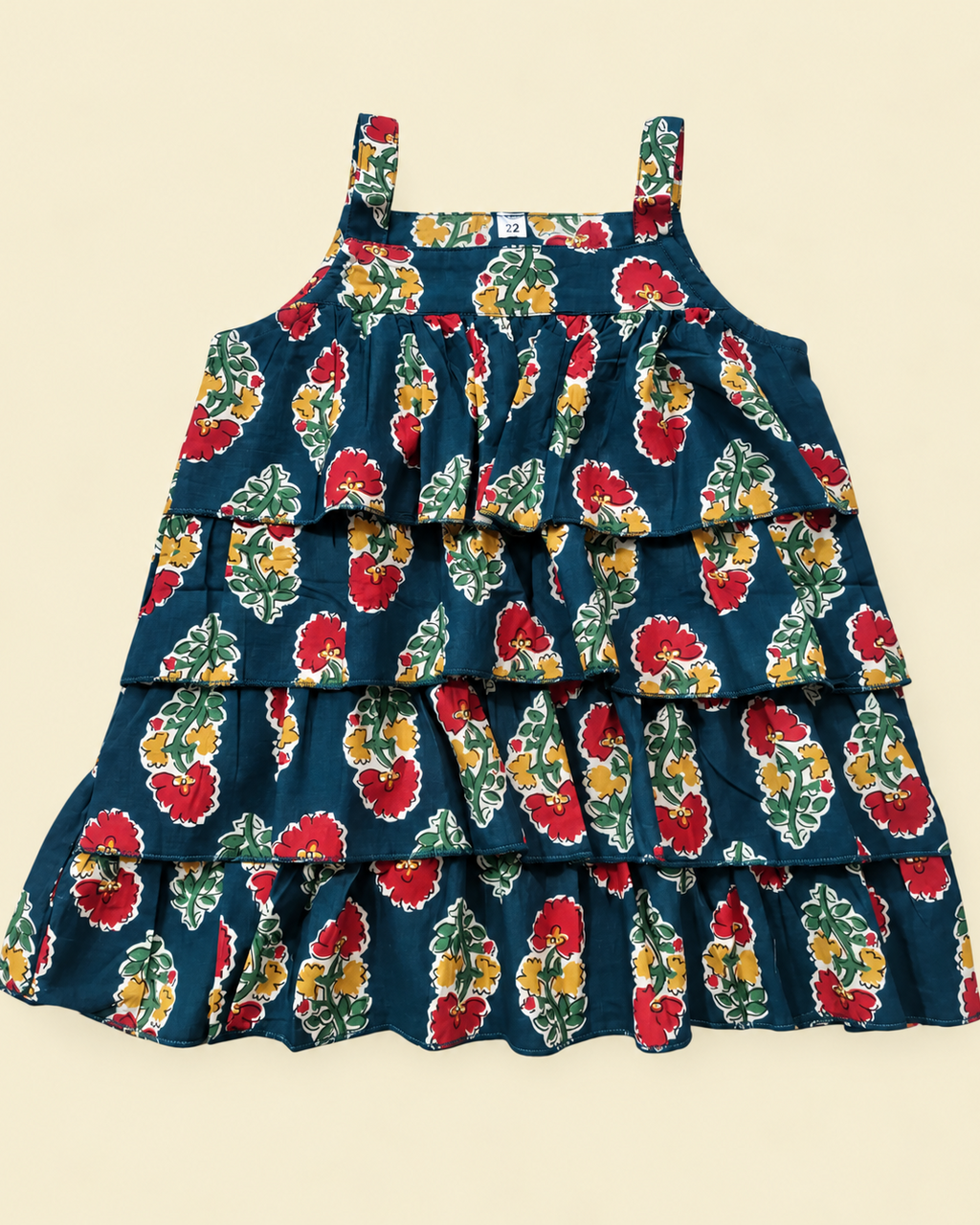 A sleeveless tiered ruffle dress with a dark teal blue background and a vibrant red, yellow, and green floral pattern, laid flat on a light beige background.