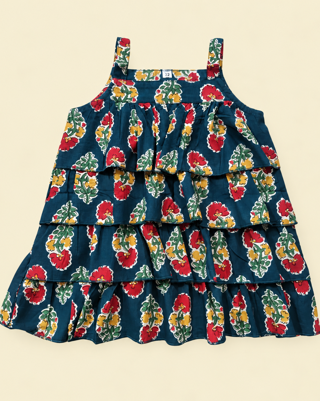 A sleeveless tiered ruffle dress with a dark teal blue background and a vibrant red, yellow, and green floral pattern, laid flat on a light beige background.