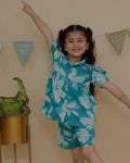 SnugBug teal floral outfit standing in a room with a beige wall and plant.