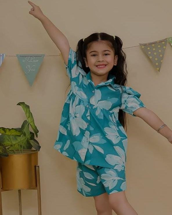SnugBug teal floral outfit standing in a room with a beige wall and plant.