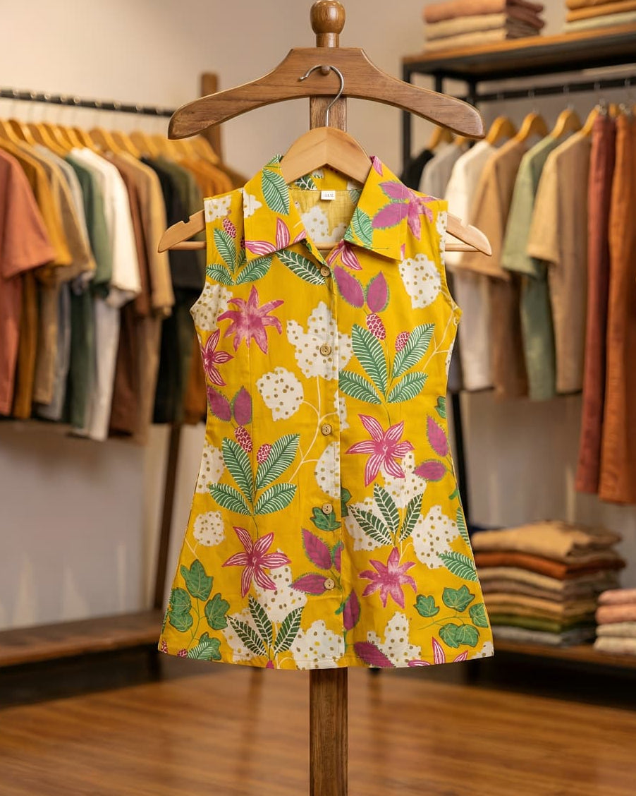 Yellow floral sleeveless shirt dress on a wooden hanger with a clothing store background.
